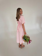Woman in a pink striped dress holding a basket of flowers against a plain background