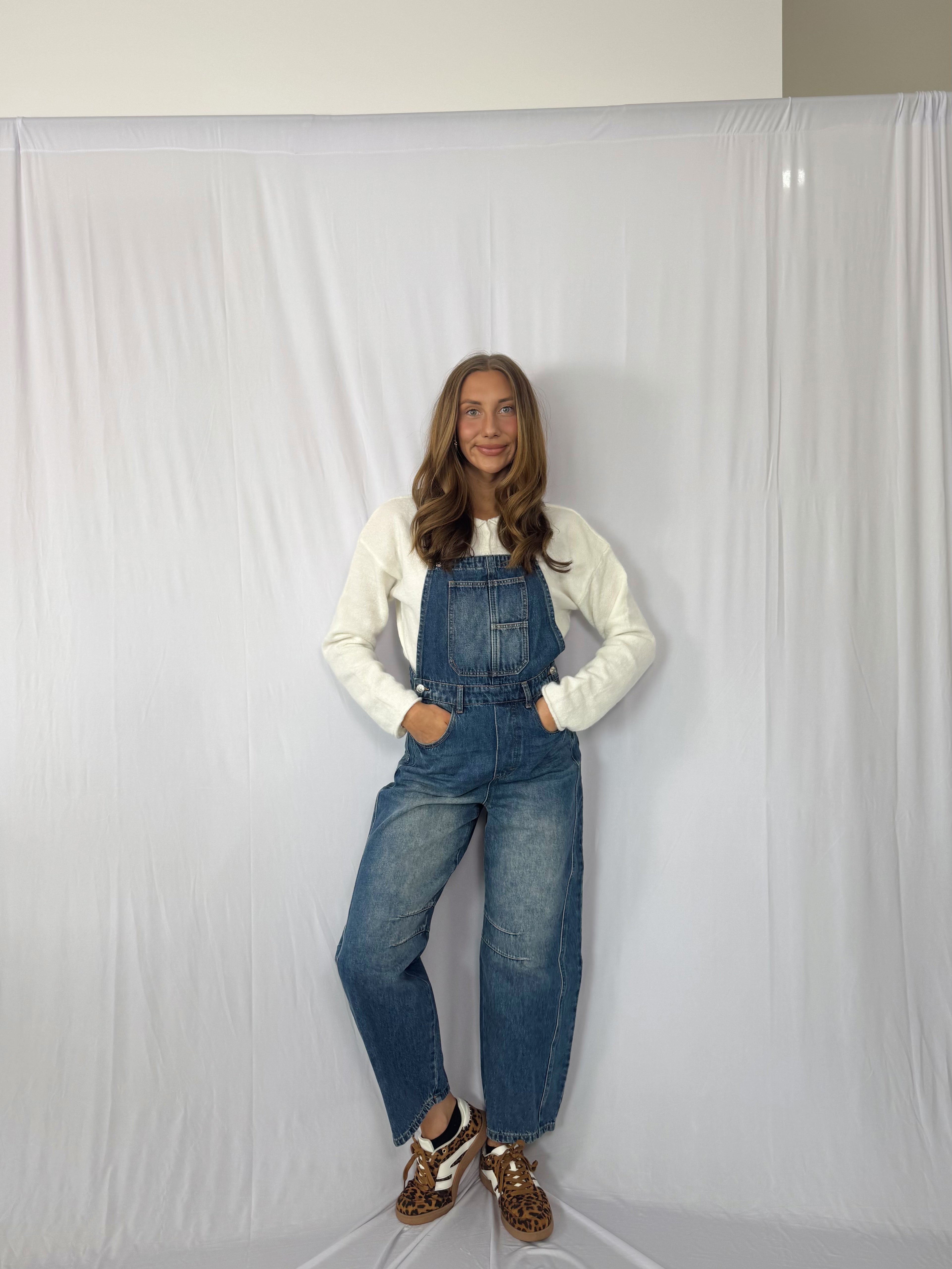 Person wearing blue denim overalls and a white long-sleeve shirt against a plain background