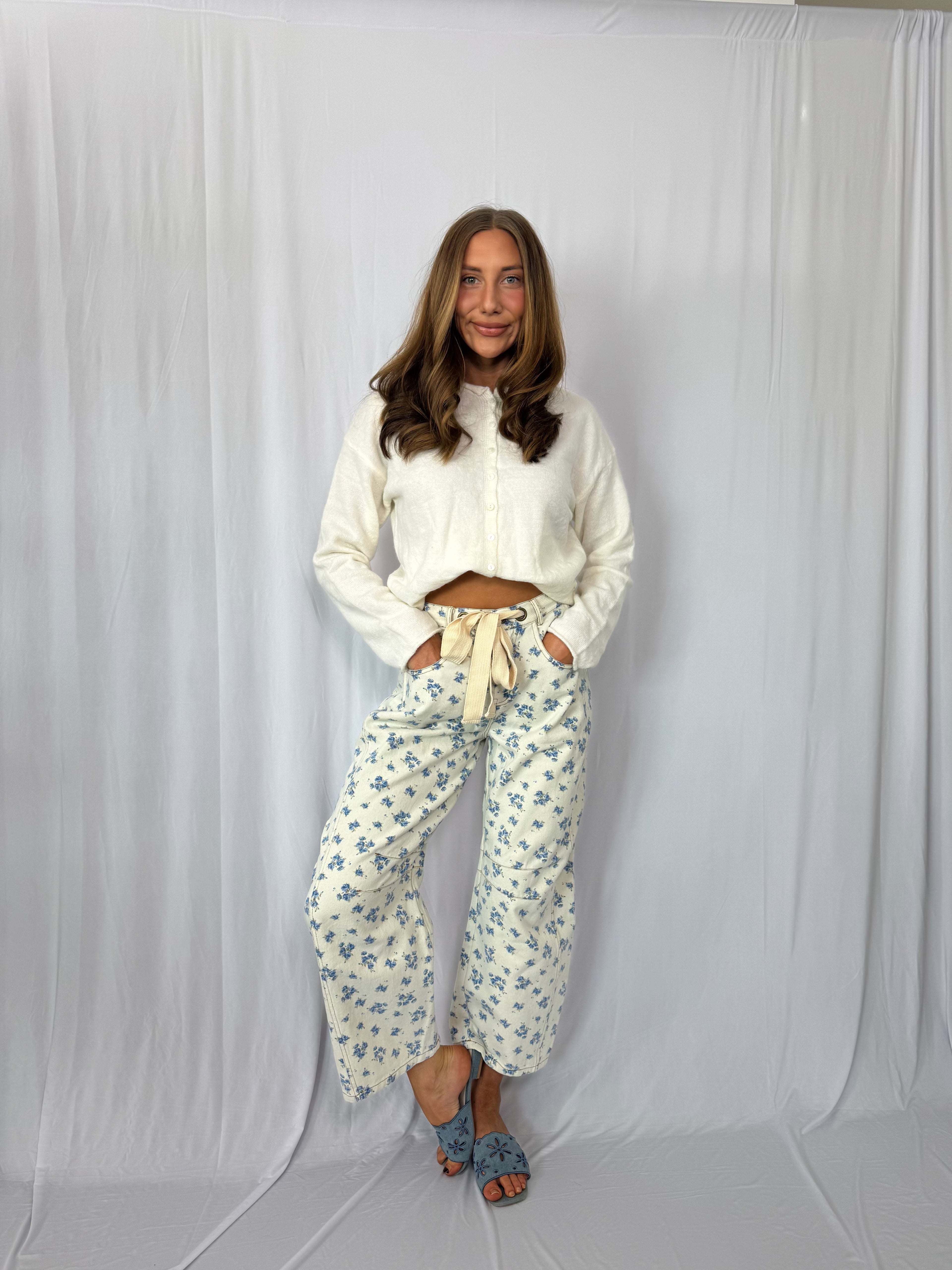 Woman wearing a white blouse and floral pants against a plain background