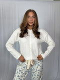 Woman wearing a white blouse and floral pants against a plain background