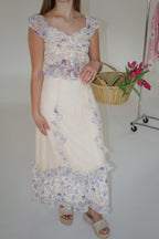 Woman wearing a floral top and white skirt holding a basket of tulips against a plain background