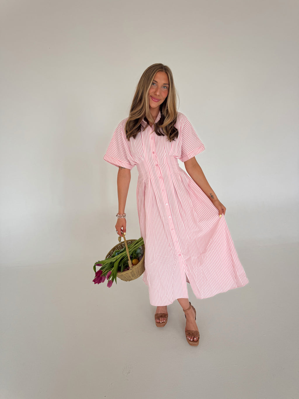 Woman wearing a pink striped dress holding a basket with flowers against a plain background