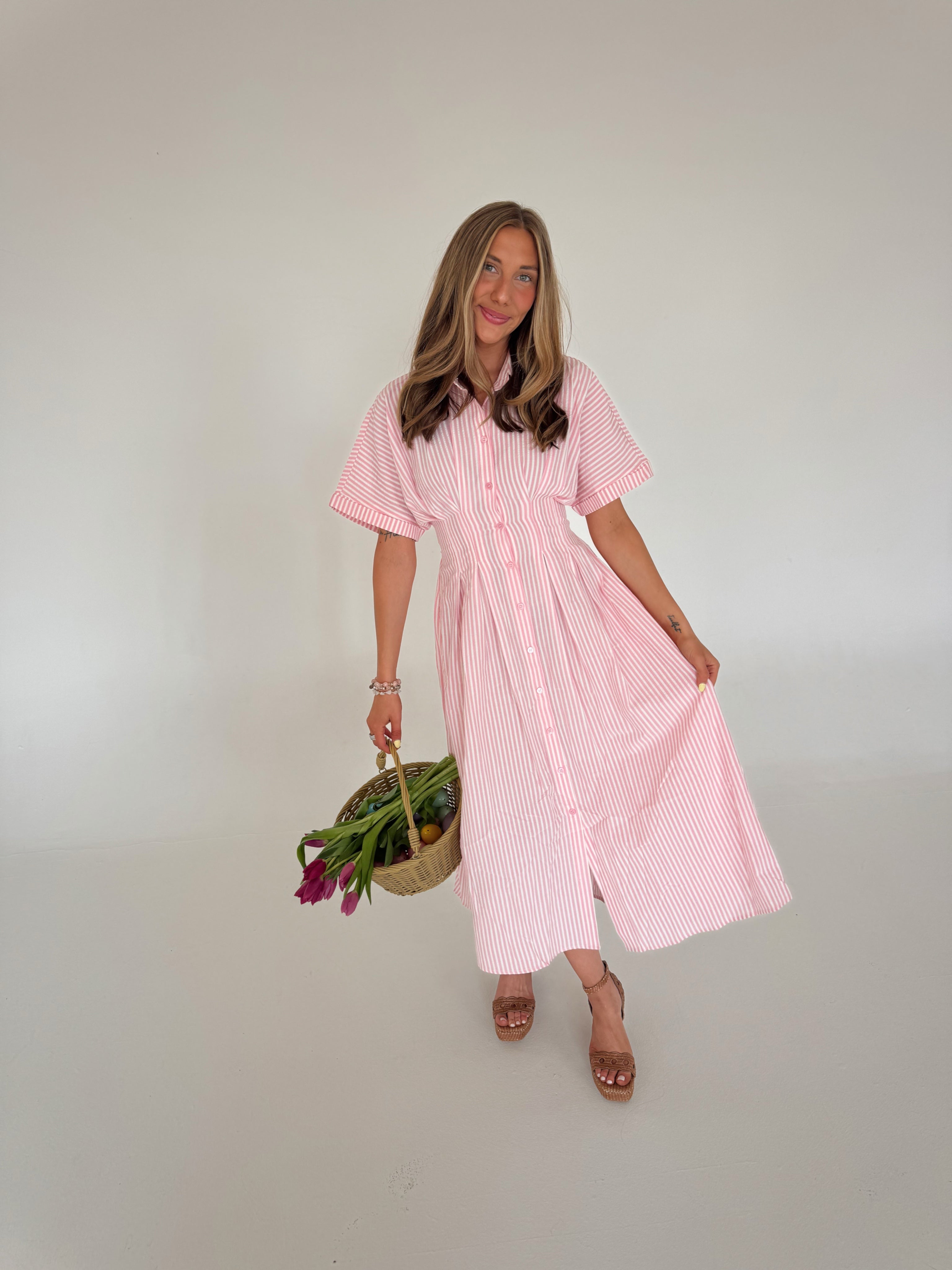 Woman wearing a pink striped dress holding a basket with flowers against a plain background