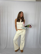 Woman in a white patterned outfit holding a tray with flowers against a white backdrop
