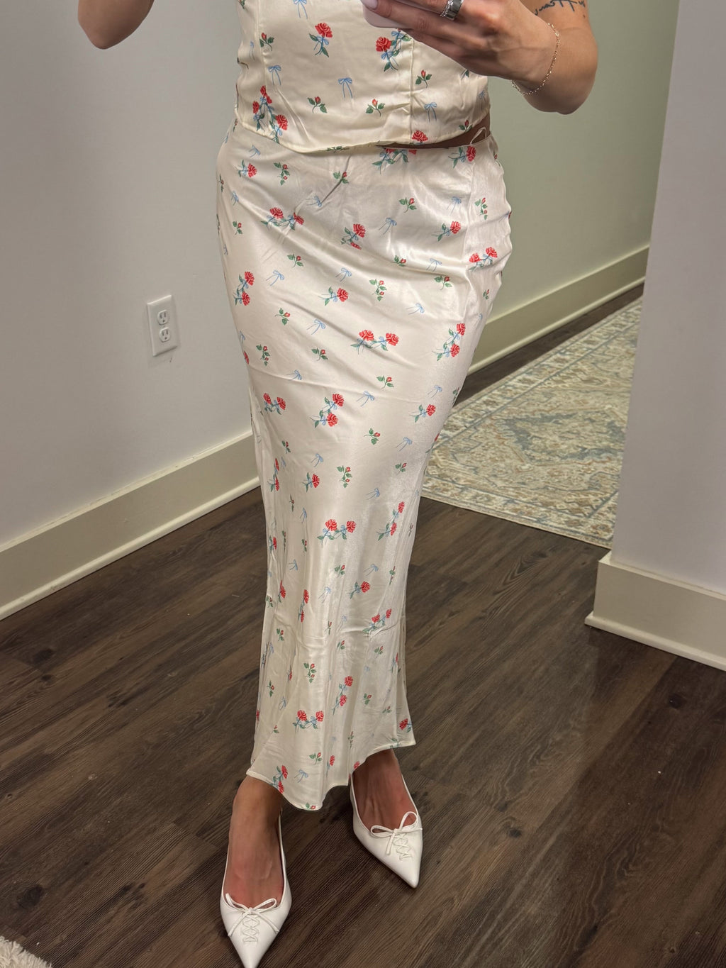 Person wearing a floral skirt standing in a room with wooden flooring.