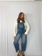 Person wearing blue denim overalls and a white long-sleeve shirt against a white background