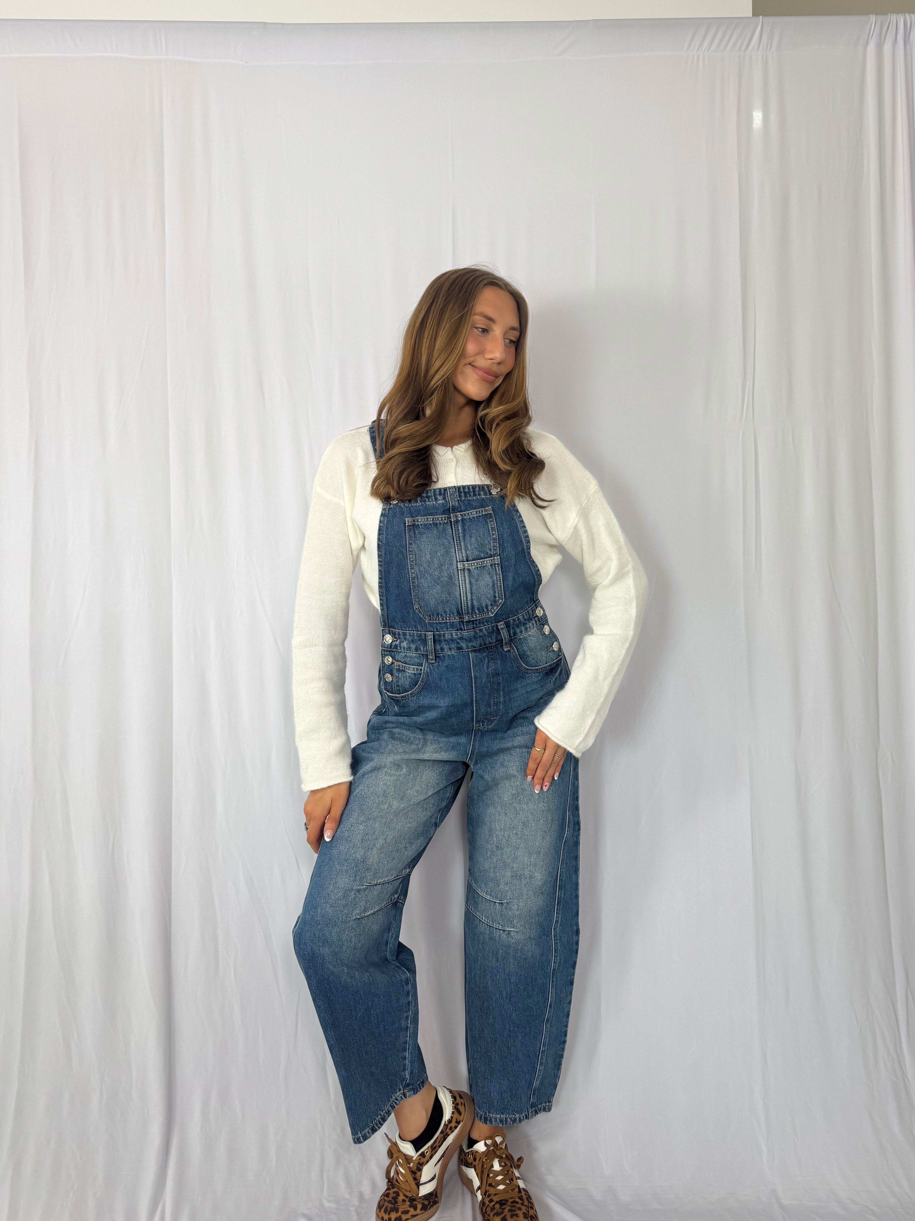 Person wearing blue denim overalls and a white long-sleeve shirt against a white background