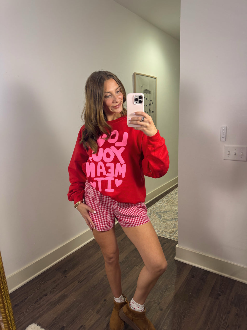Person wearing a red sweatshirt and pink checkered shorts taking a mirror selfie.