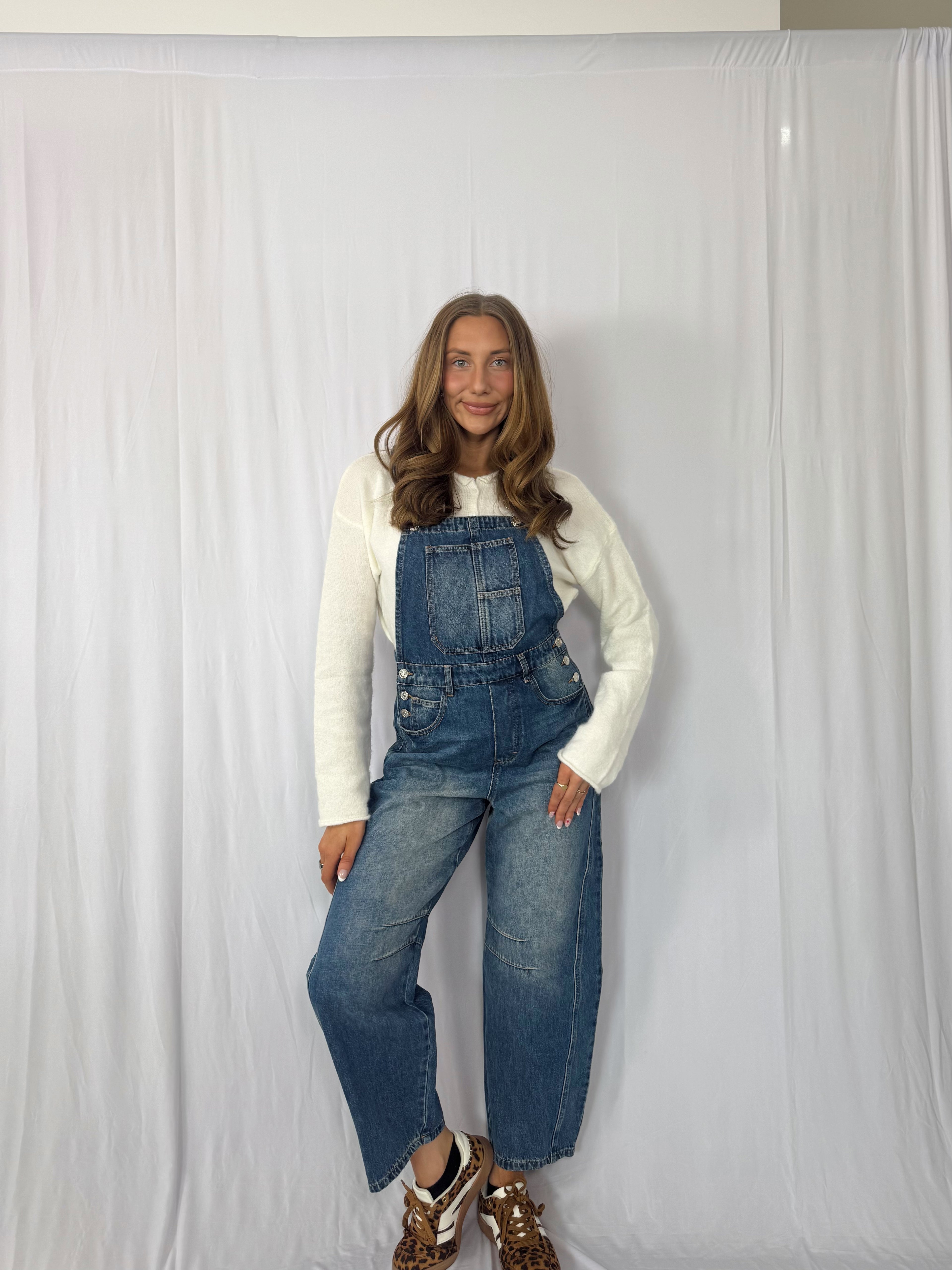 Woman wearing blue denim overalls against a white background