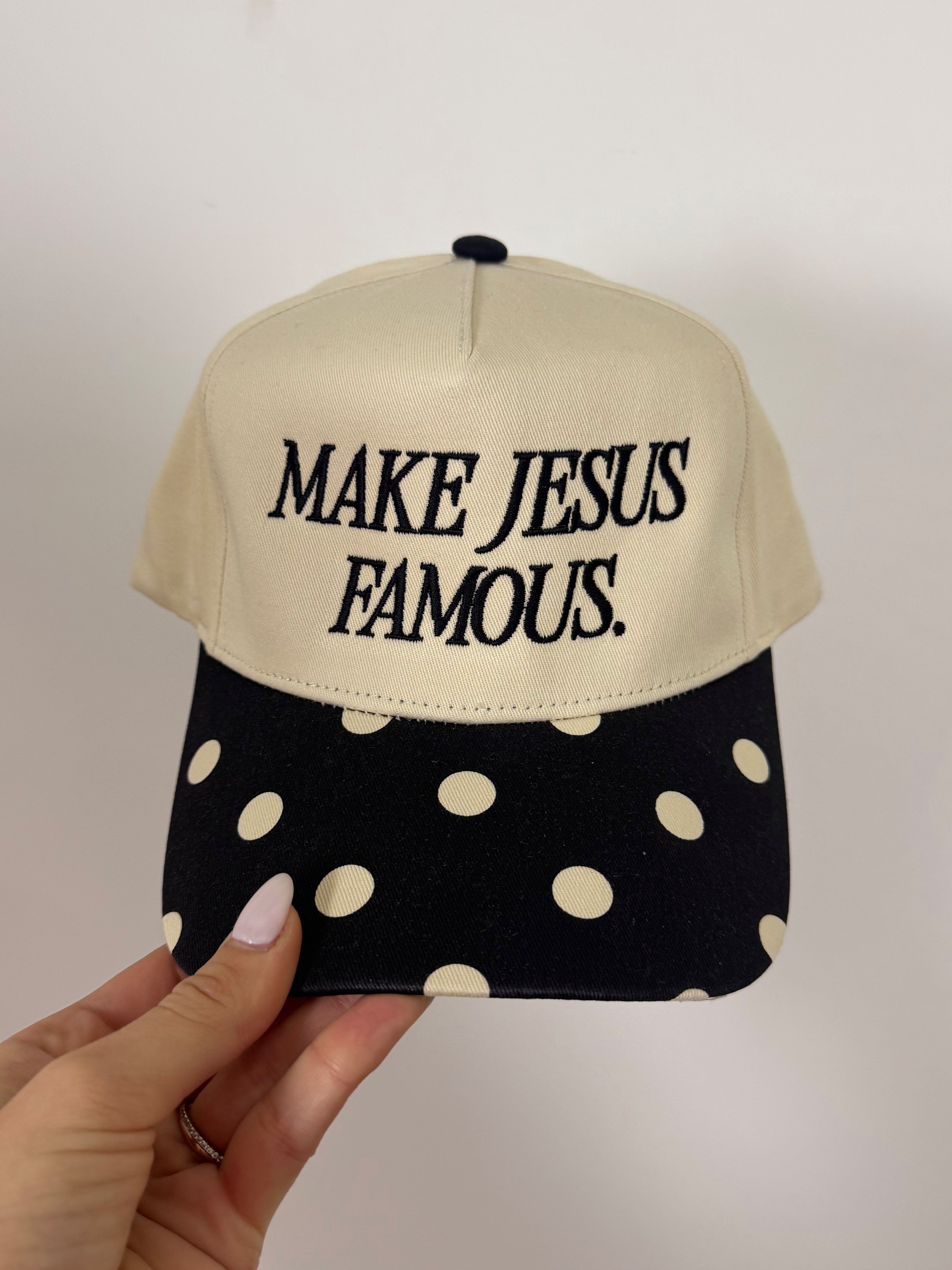 Cap with 'MAKE JESUS FAMOUS.' text on beige top and polka dot black bottom, held by a hand.