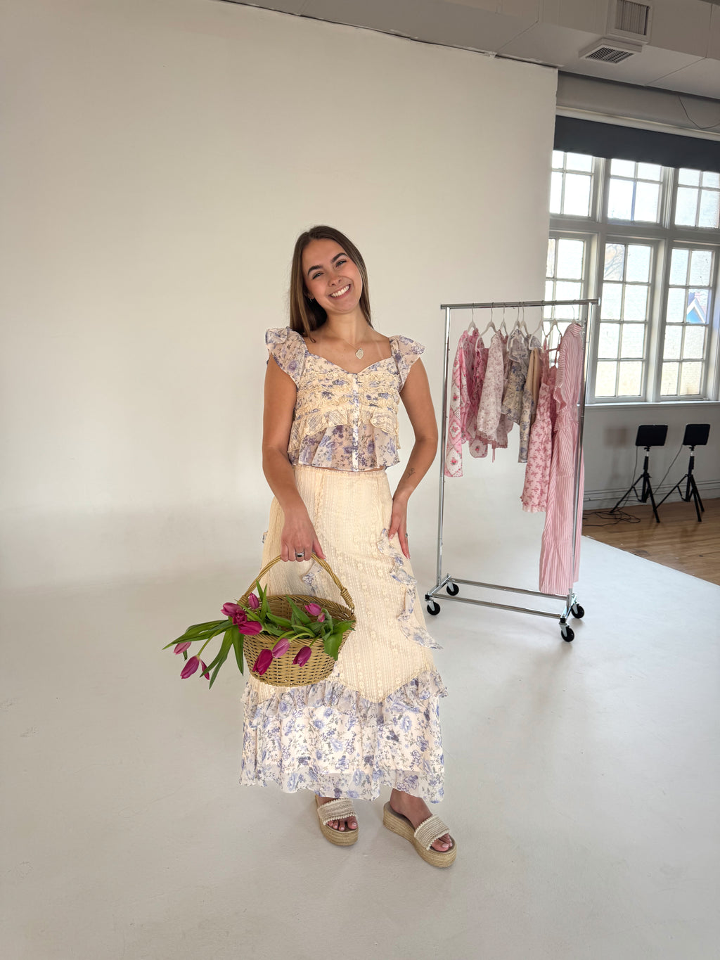 Woman holding a basket of flowers in a room with clothing racks.
