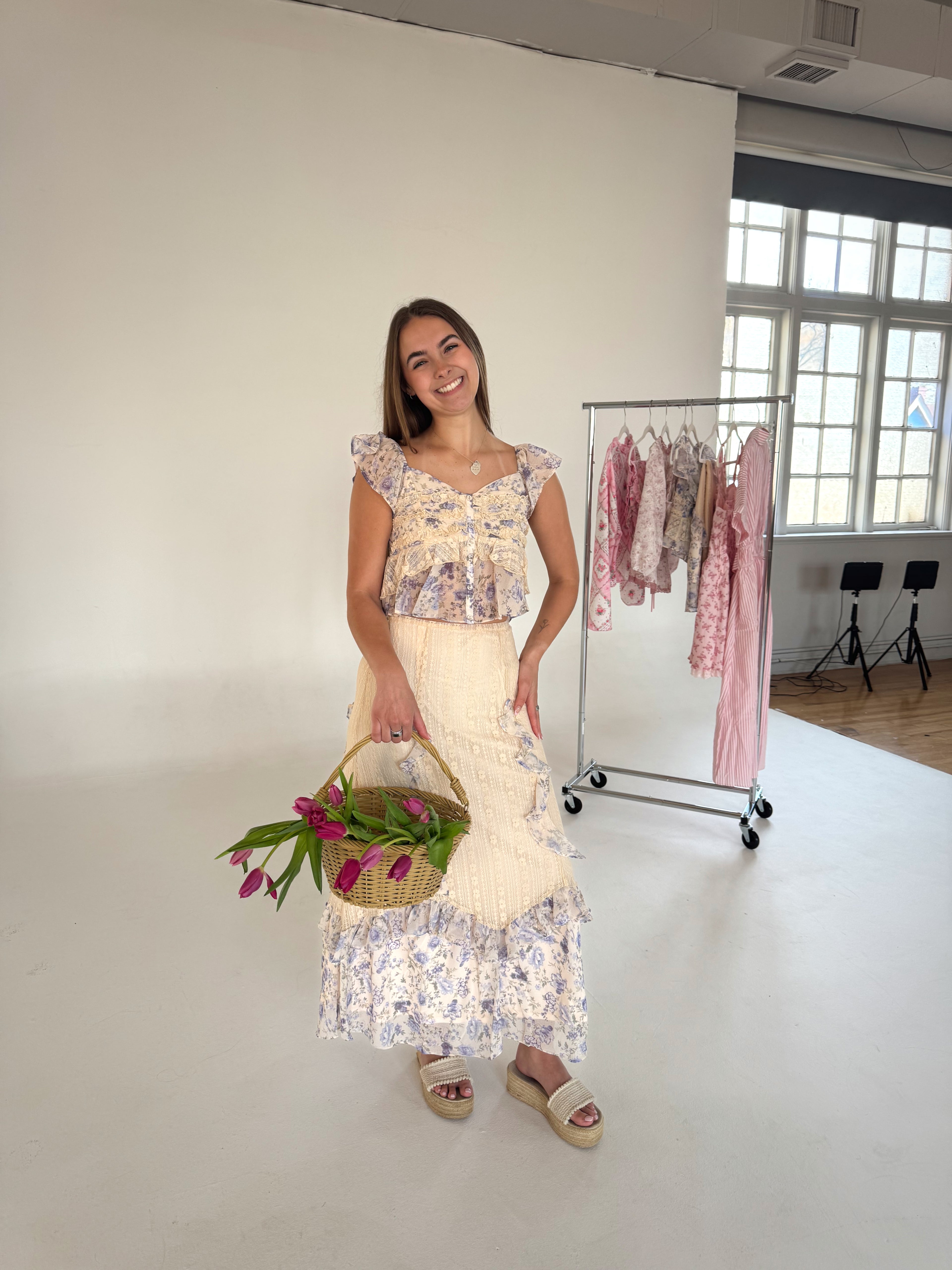 Woman holding a basket of flowers in a room with clothing racks.