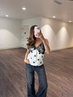 Woman taking a mirror selfie of a white top with black polka dots in a room with wooden flooring and white walls.