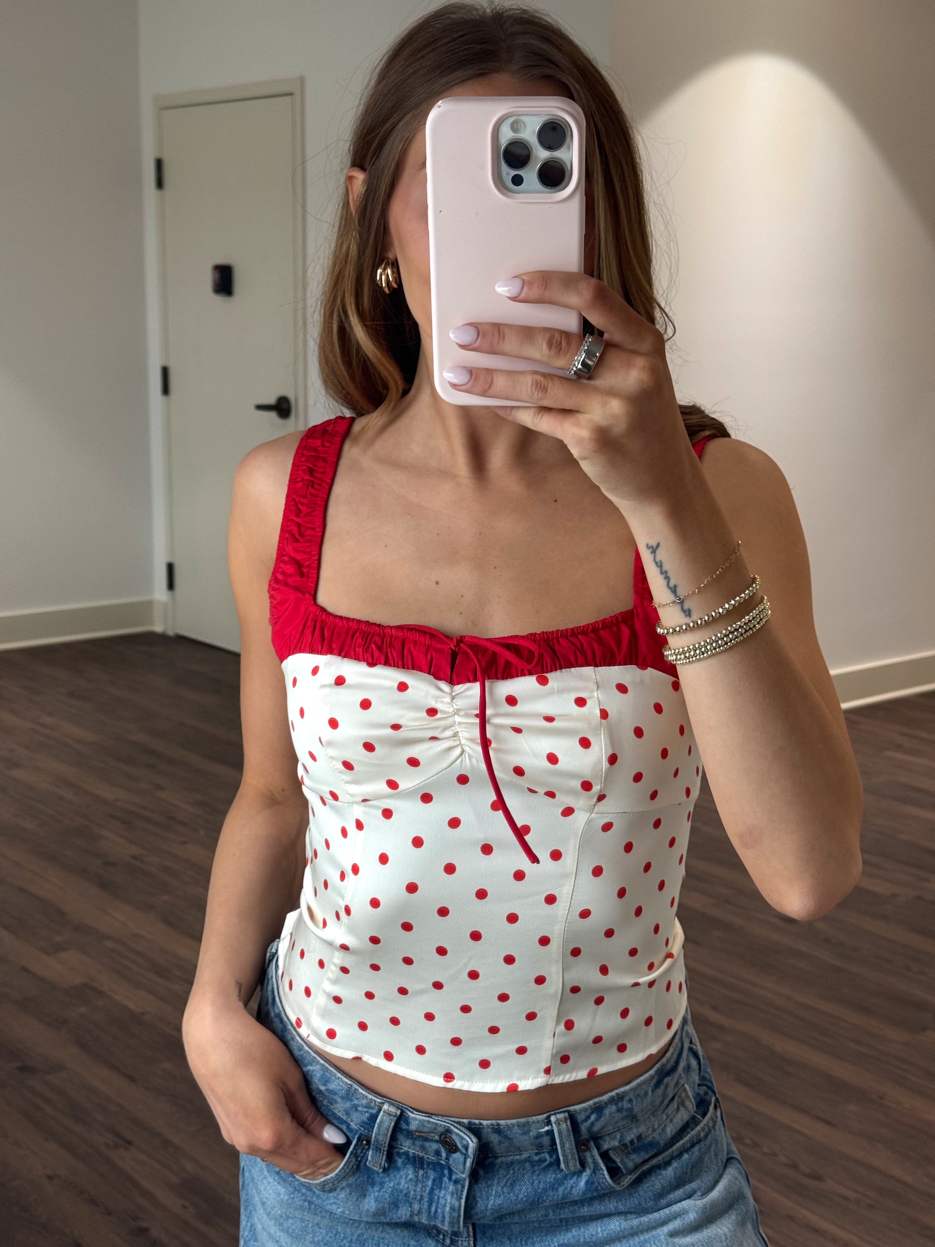Person wearing a red and white polka dot top taking a mirror selfie.