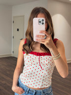 Person wearing a white top with red polka dots and blue jeans, taking a mirror selfie.