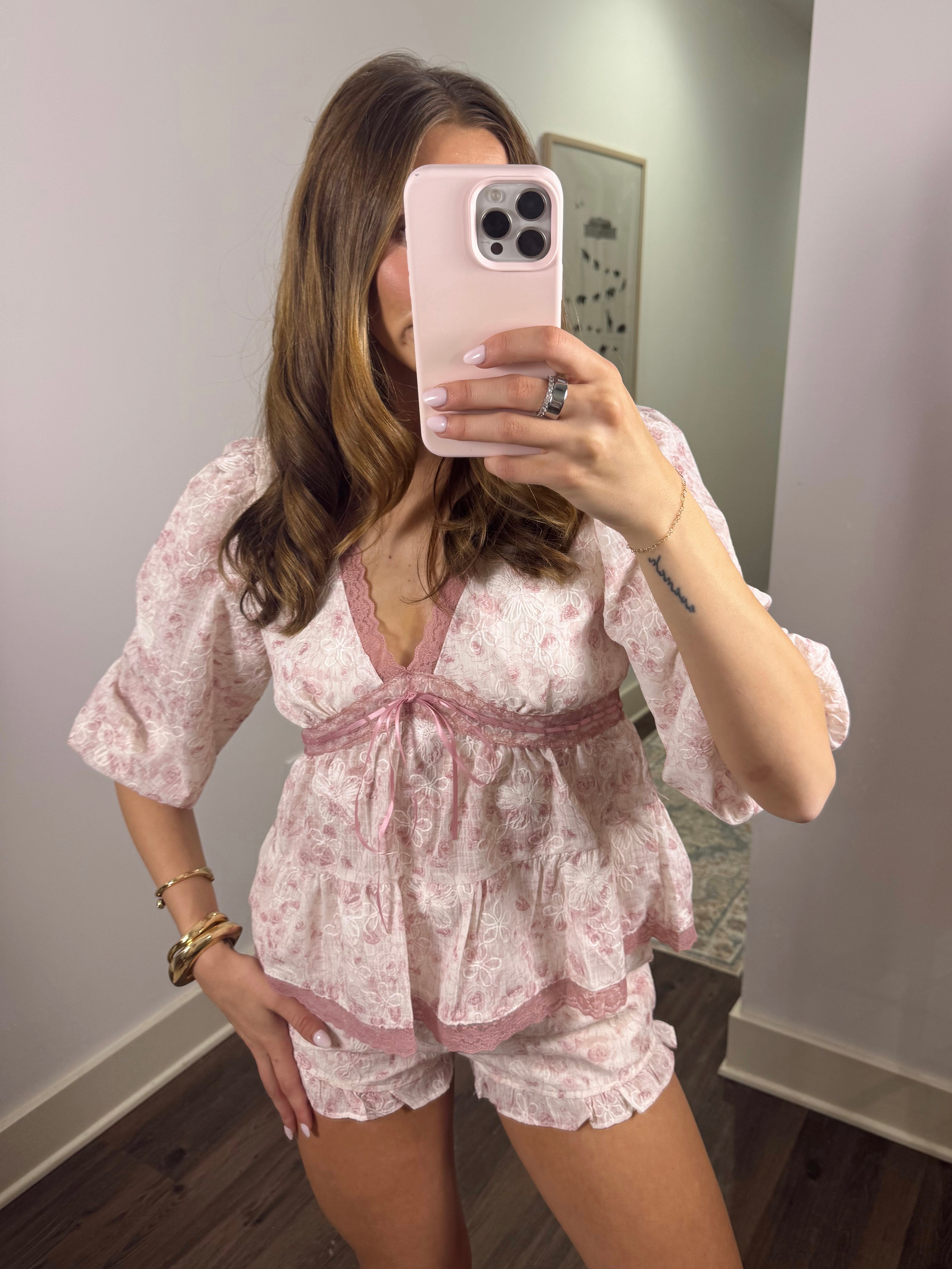 Woman taking a mirror selfie wearing a pink lace short set.