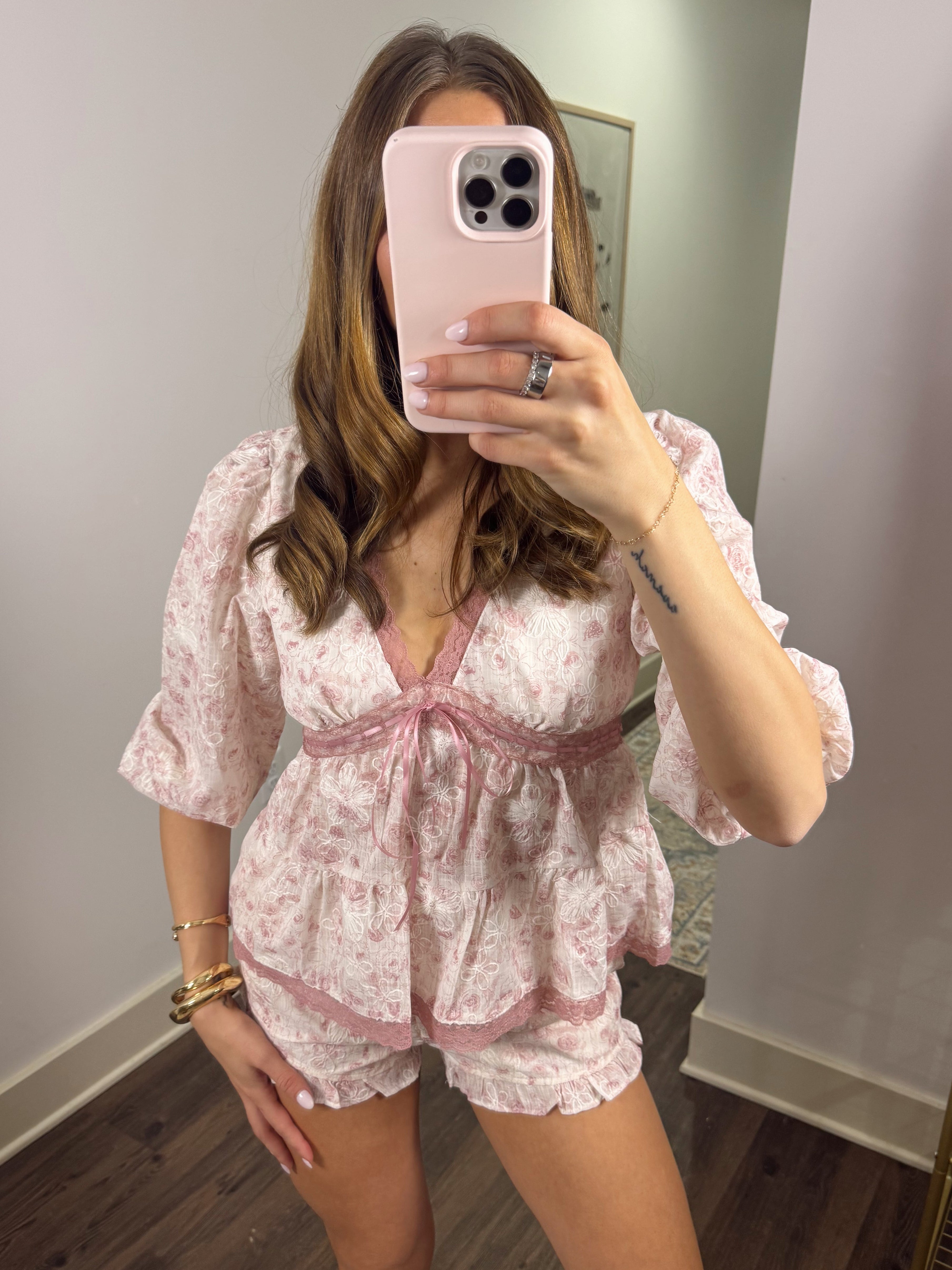 Woman taking a mirror selfie wearing a pink floral short set in a room.