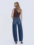 Woman wearing dark blue barrel jeans and a brown top on a white background