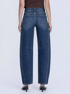 Person wearing dark blue barrel jeans on a white background