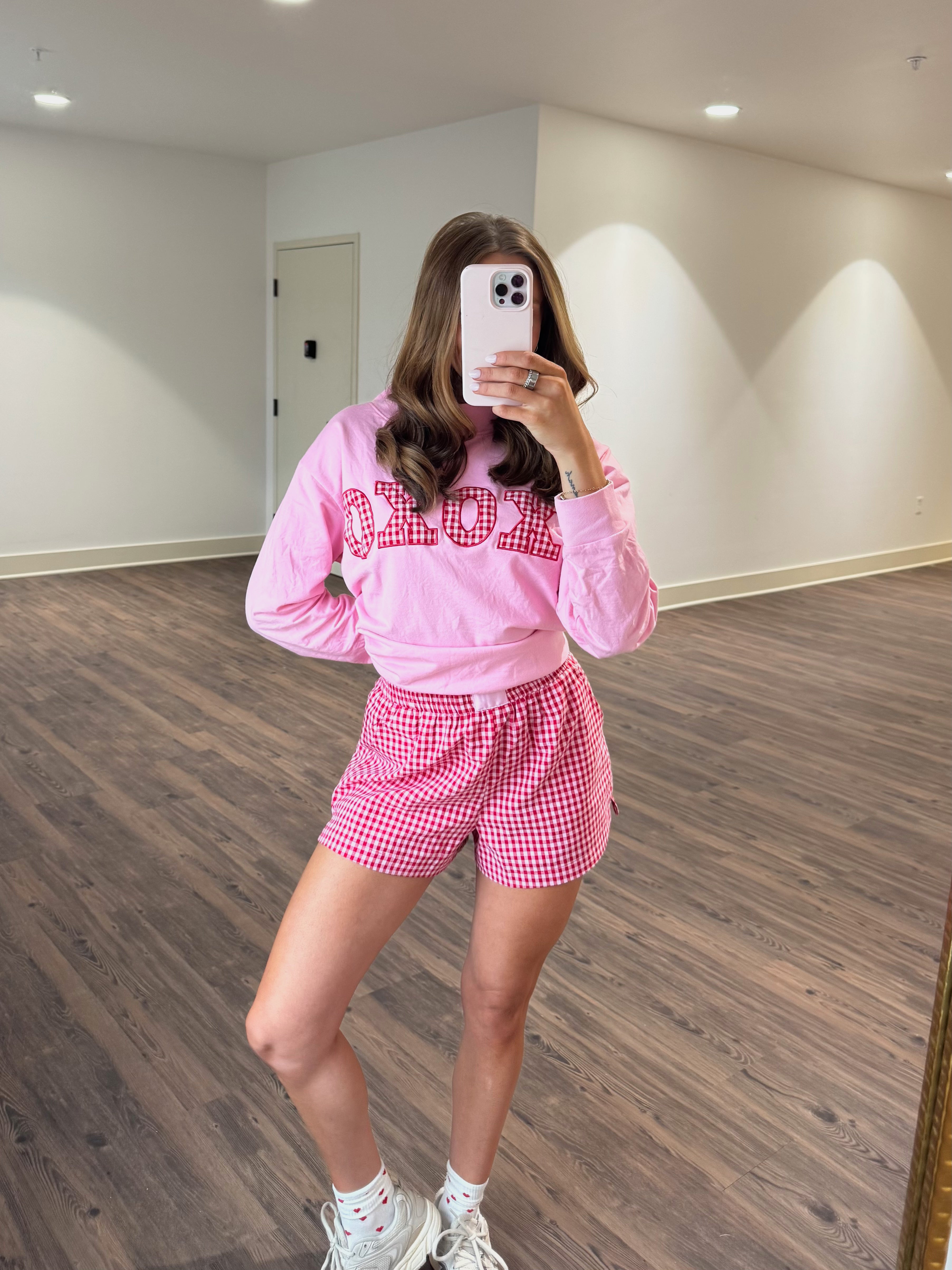 Person wearing a pink sweatshirt with text and red checkered shorts in a room.