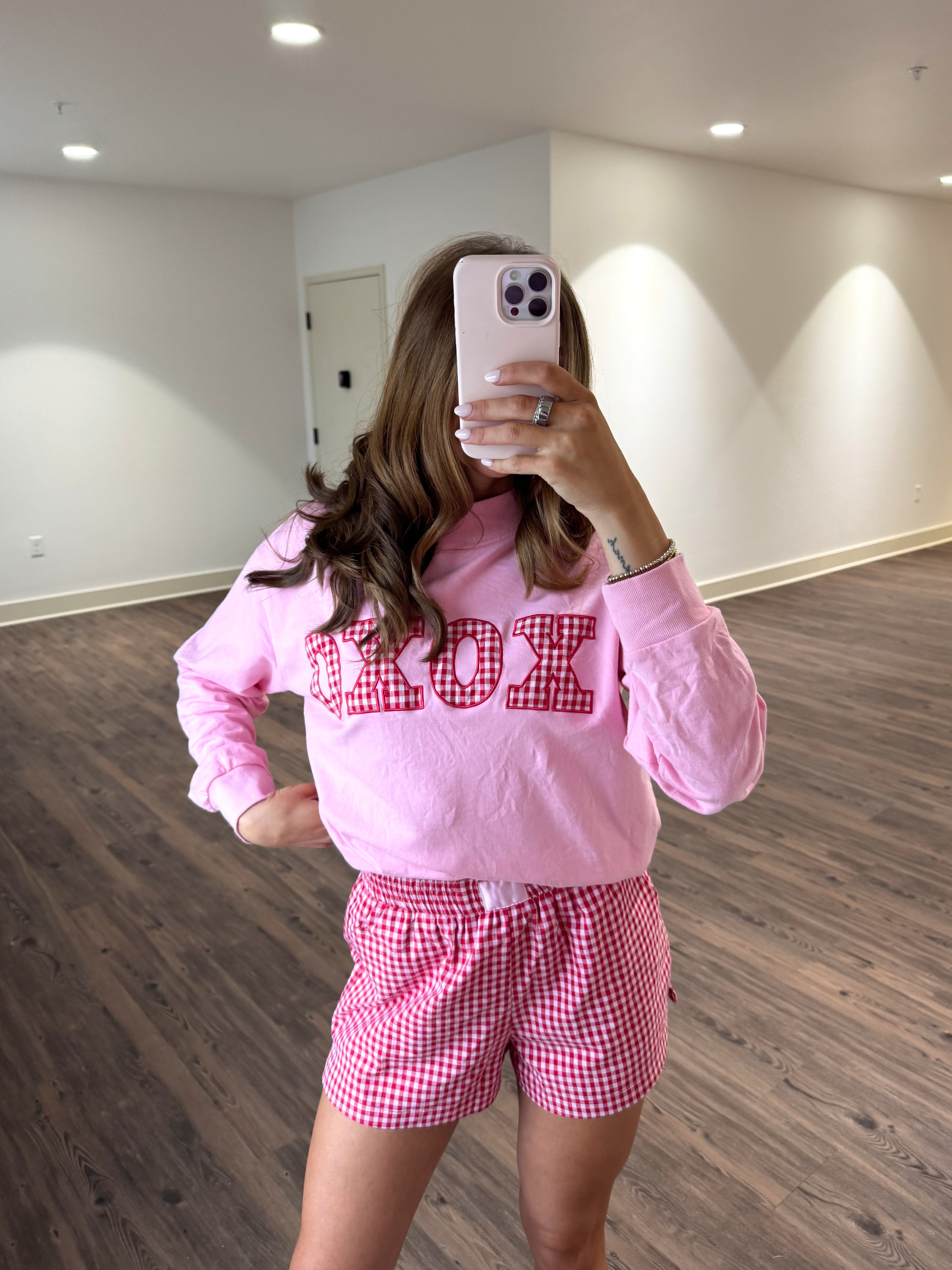 Person wearing a pink sweatshirt with text and red checkered shorts in a room.